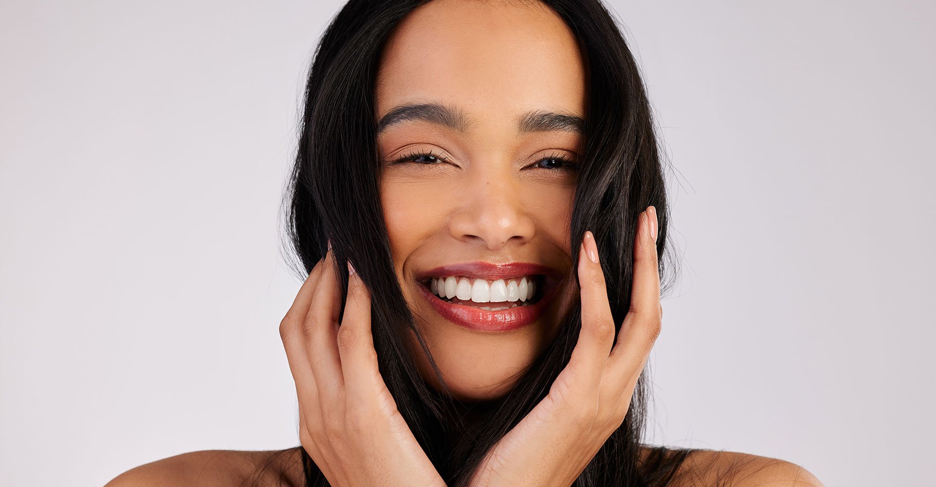 Mulher sorri ao tocar seus cabelos saudáveis com os cuidados necessários e tônico capilar