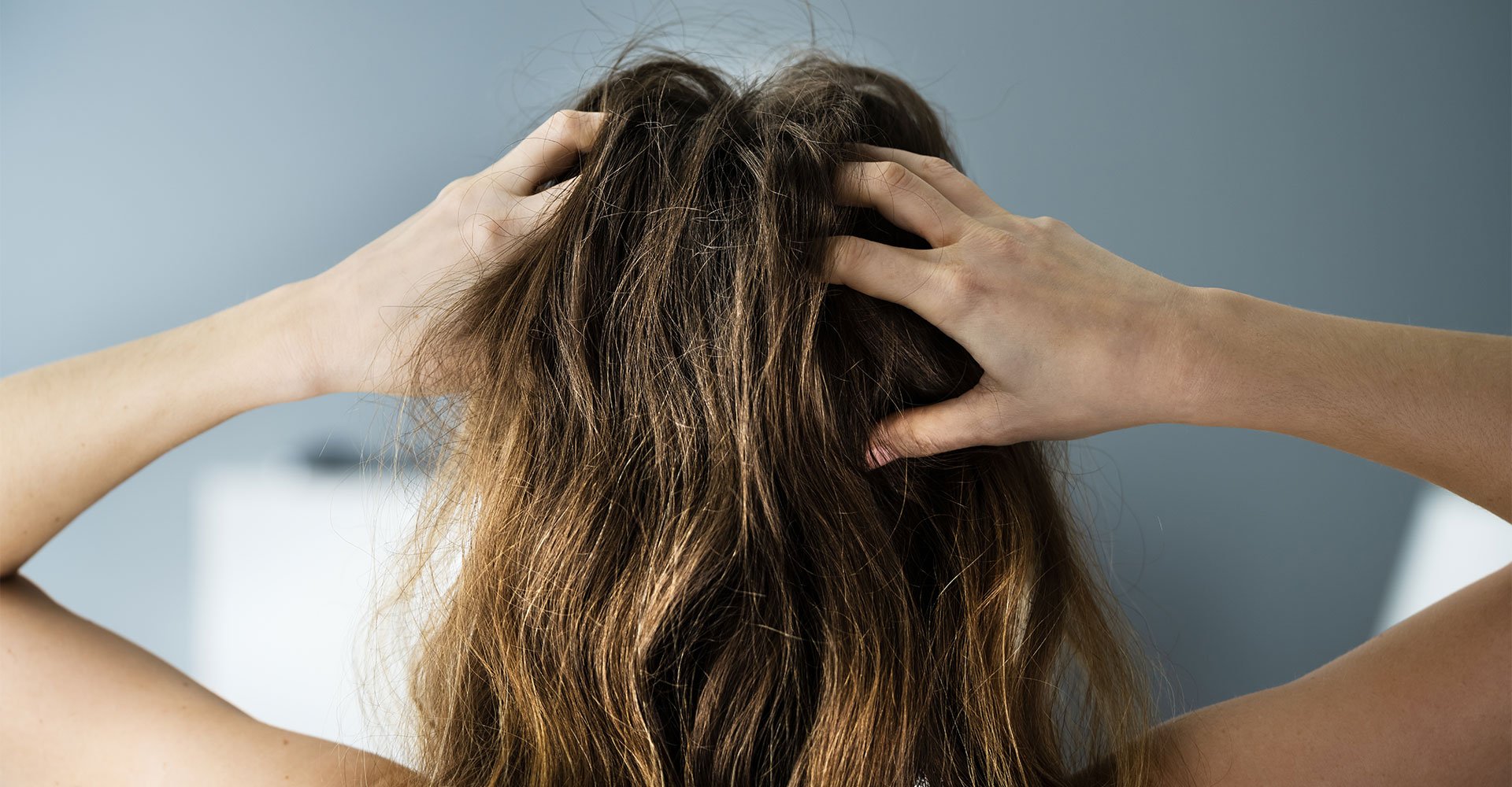 Mulher com cabelo castanho claro colocando as mãos no cabelo danificado