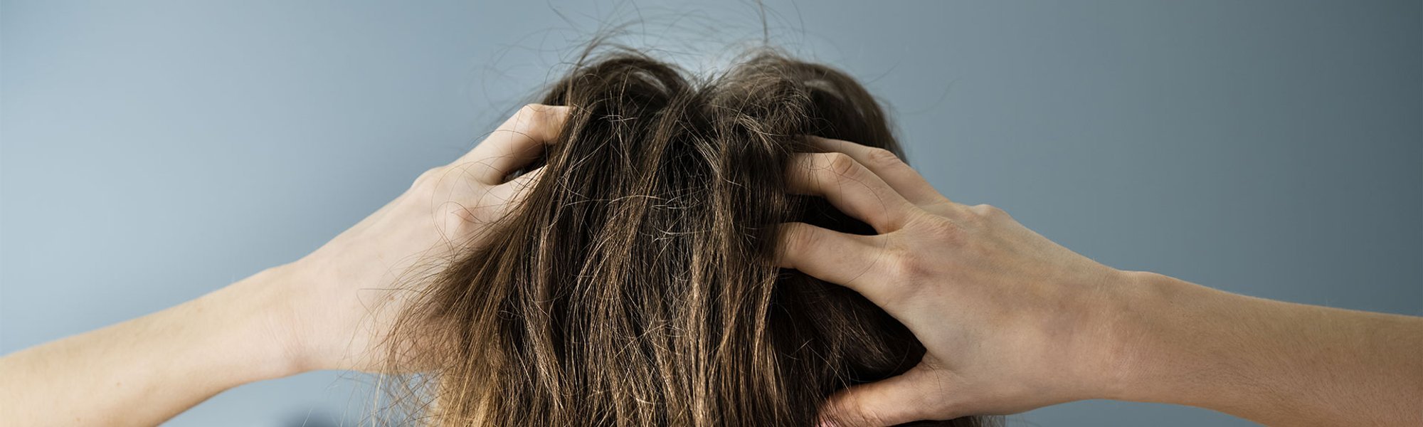 Mulher com cabelo castanho claro colocando as mãos no cabelo danificado