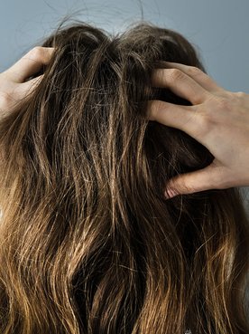 Mulher com cabelo castanho claro colocando as mãos no cabelo danificado