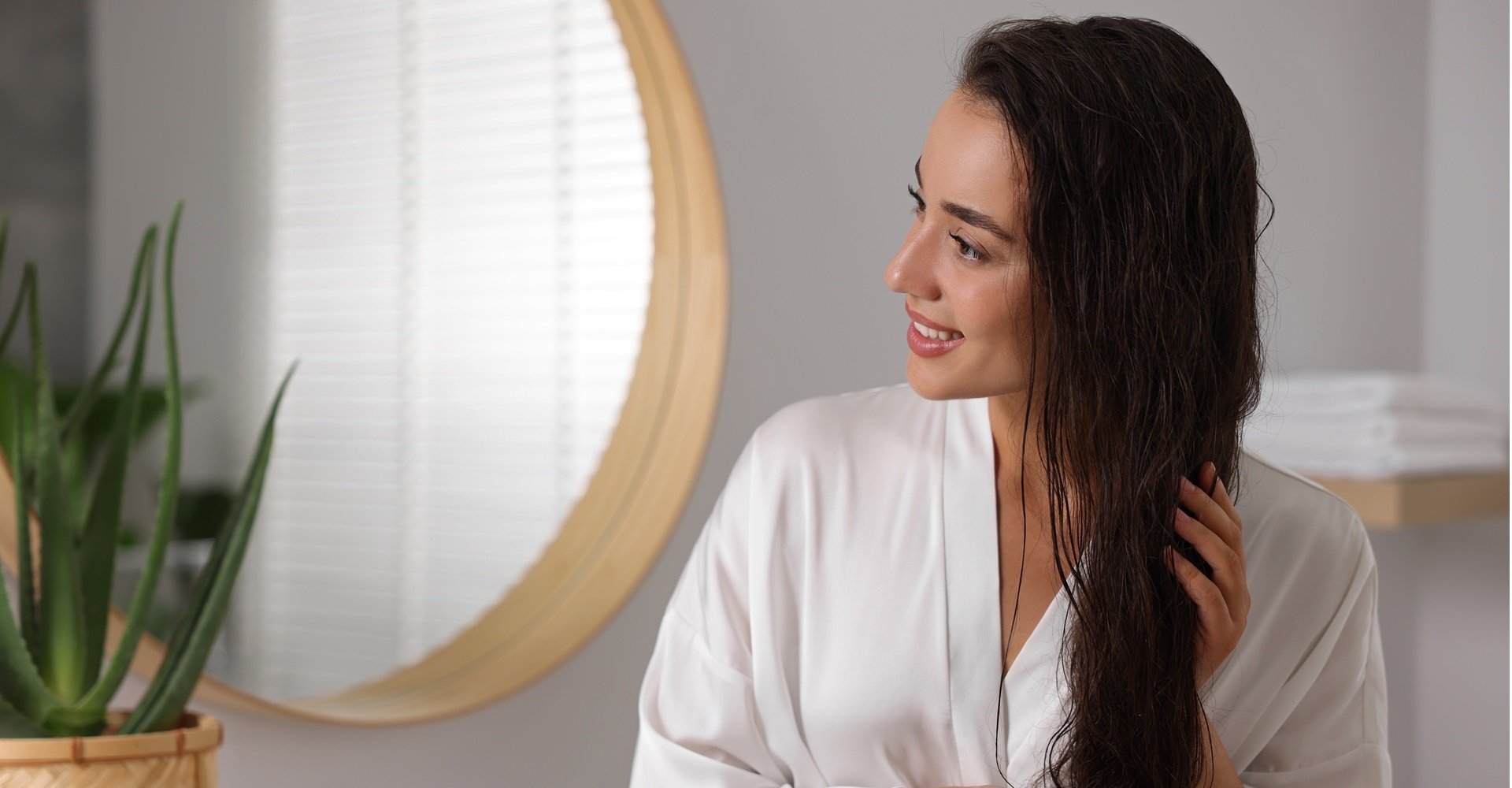 Mulher sorridente com cabelo castanho cuidando dos cabelos em um banheiro.