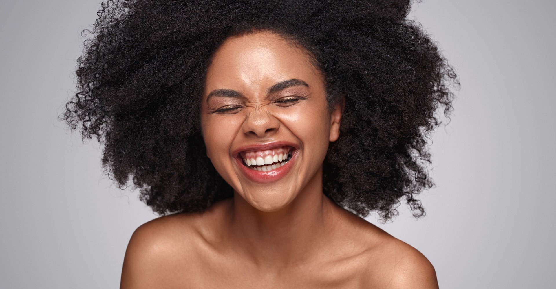 mulher de pele negra com cabelo crespo posando para a foto sorridente