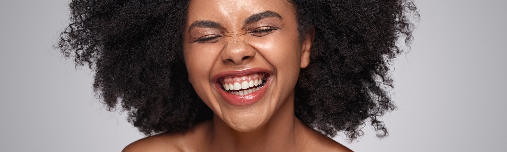 mulher de pele negra com cabelo crespo posando para a foto sorridente