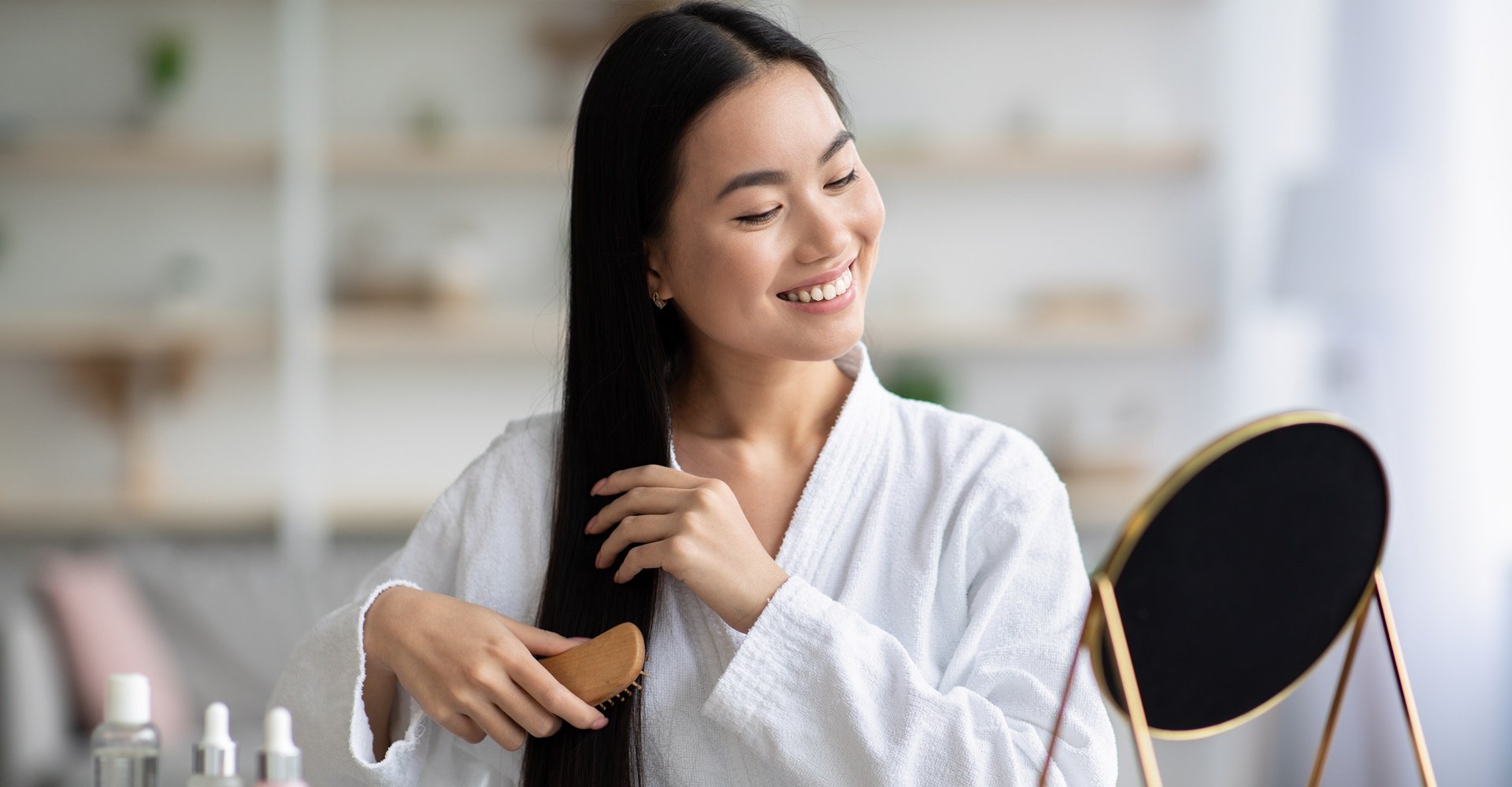 Mulher sorrindo com roupão branco enquanto penteia o cabelo após usar manteiga de karité nos fios.