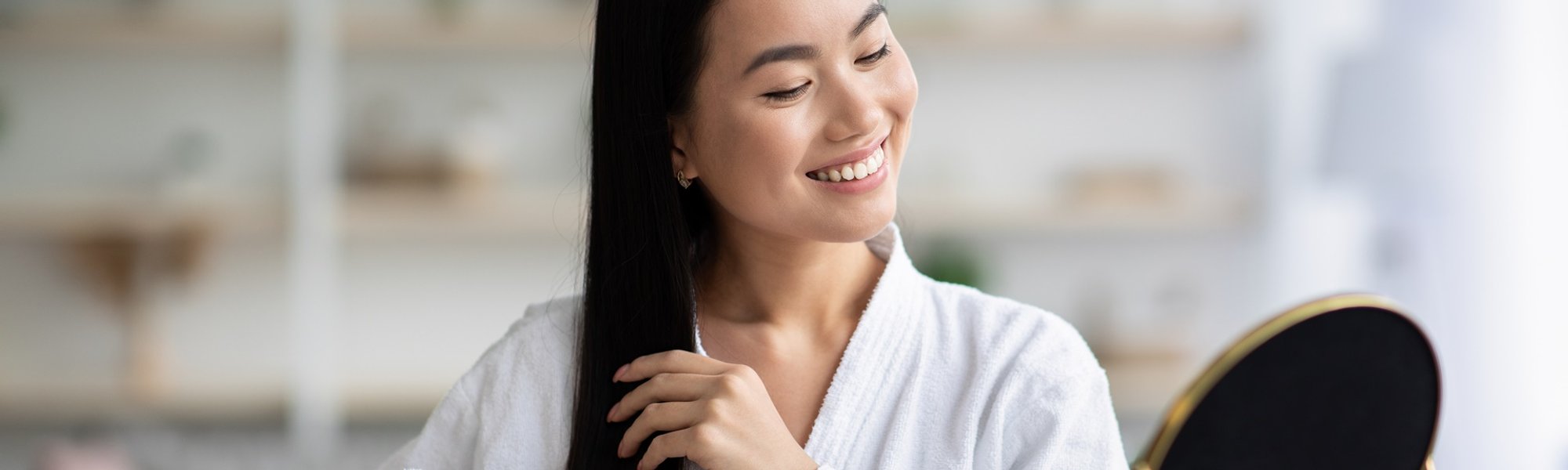 Mulher sorrindo com roupão branco enquanto penteia o cabelo após usar manteiga de karité nos fios.