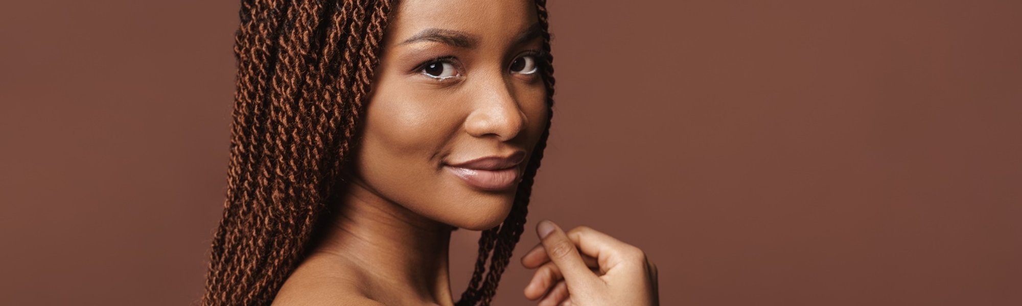 Mulher negra com trança twist no cabelo castanho olhando para a câmera em fundo marrom.