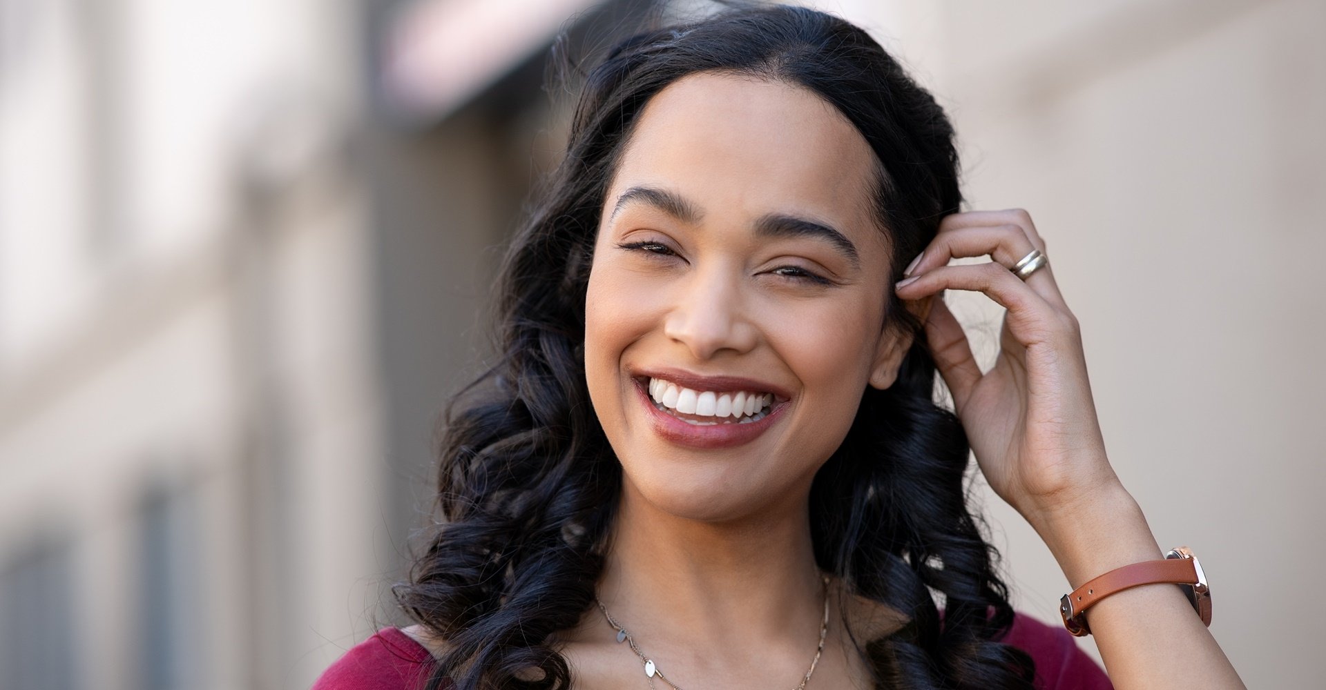 Mulher sorri ao tocar seu cabelo escuro que pode ser clareado