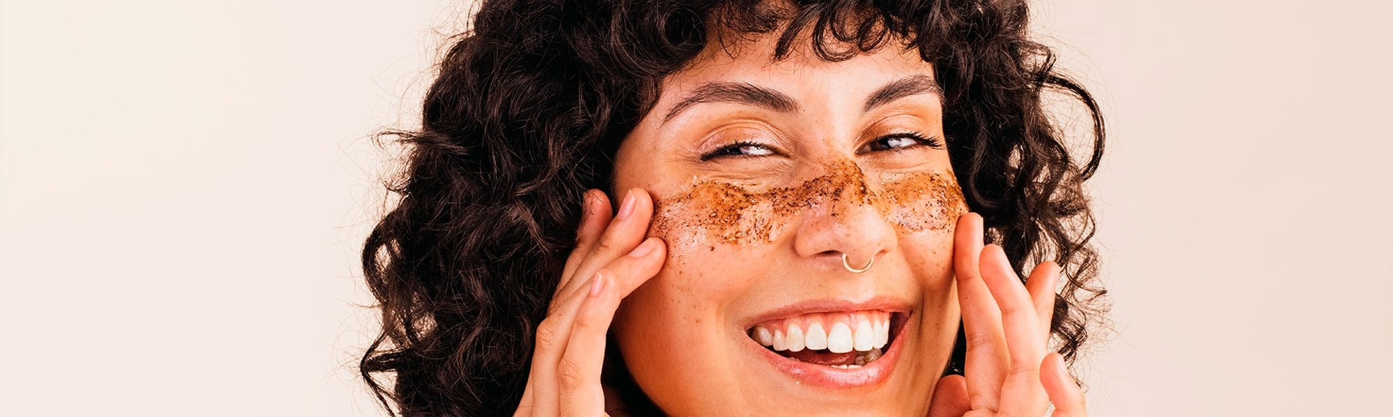 Mulher sorri ao utilizar esfoliante facial