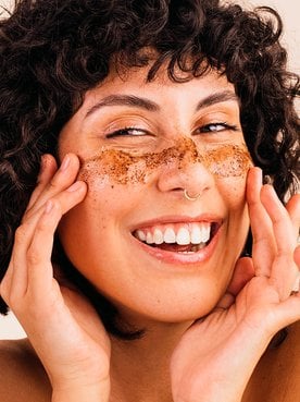 Mulher sorri ao utilizar esfoliante facial