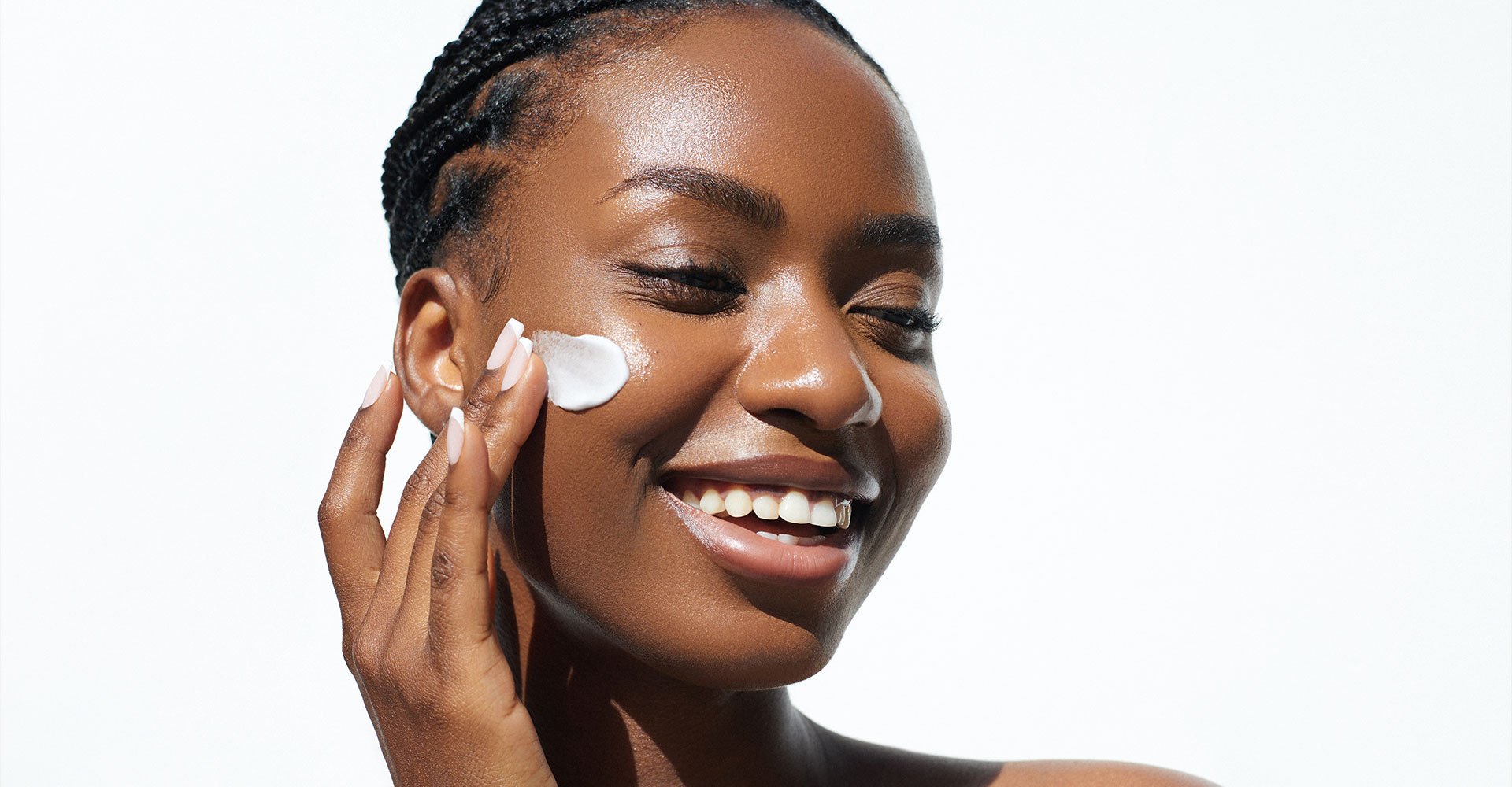 Mulher negra sorrindo e com olhos fechados aplicando creme com niacinamida no rosto