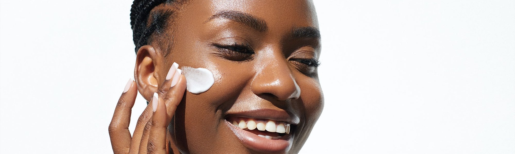 Mulher negra sorrindo e com olhos fechados aplicando creme com niacinamida no rosto