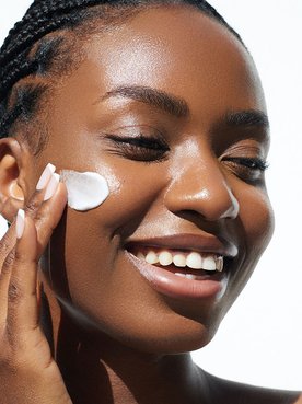 Mulher negra sorrindo e com olhos fechados aplicando creme com niacinamida no rosto