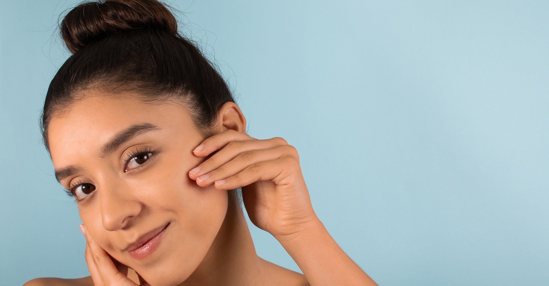 Mulher jovem toca seu rosto que tem uma pele saudável e lisa