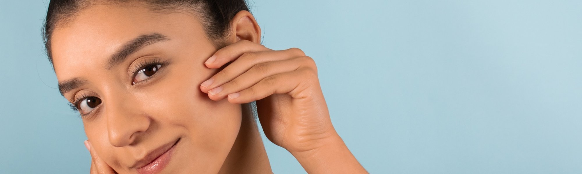 Mulher jovem toca seu rosto que tem uma pele saudável e lisa