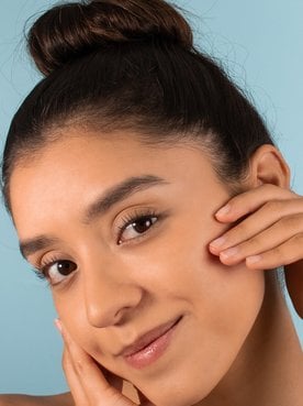 Mulher jovem toca seu rosto que tem uma pele saudável e lisa