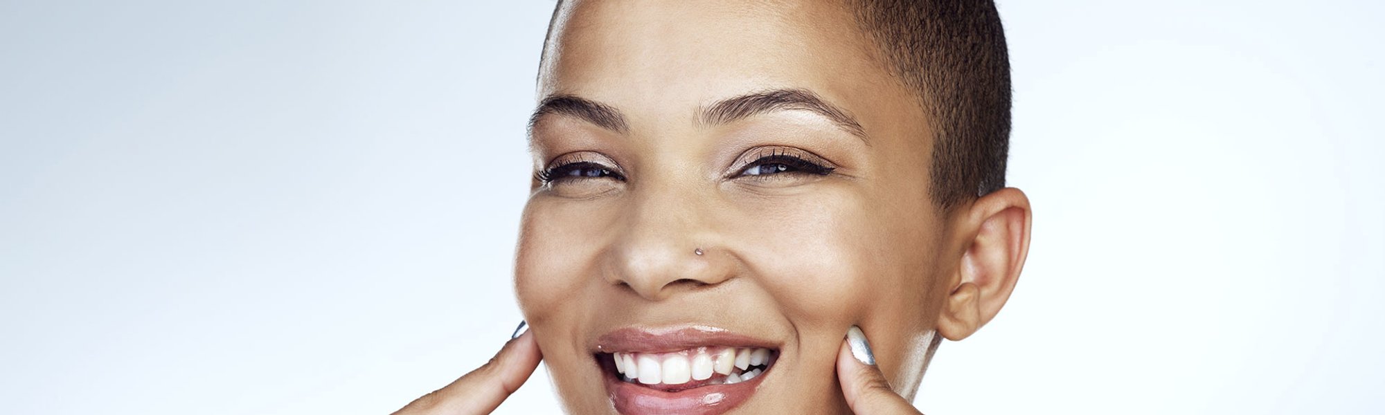 mulher negra sorrindo para a foto com os dedos levemente apoiados no rosto