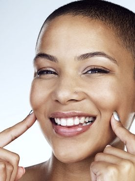 mulher negra sorrindo para a foto com os dedos levemente apoiados no rosto