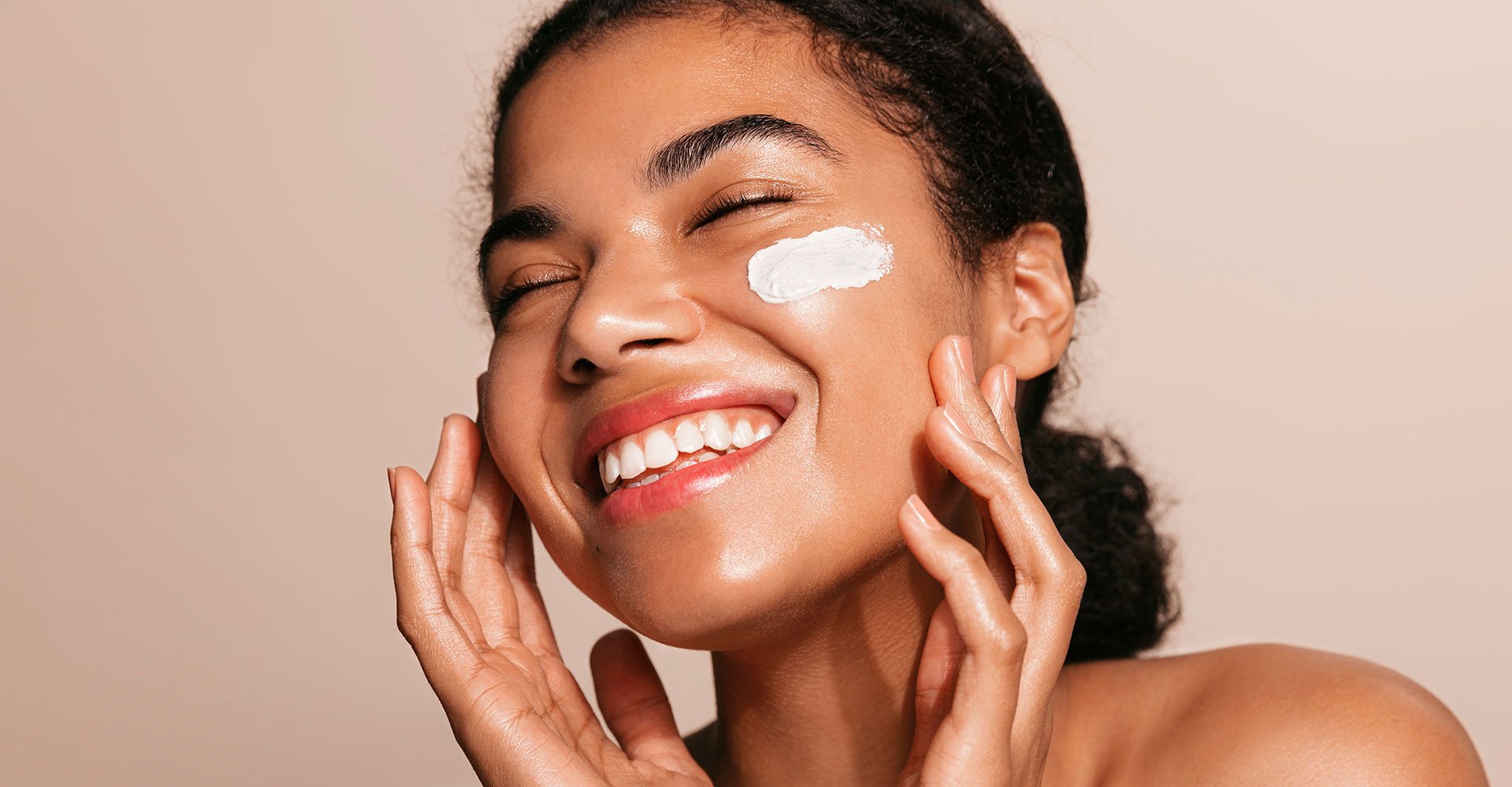 Mulher negra sorrindo com olho fechado e protetor solar facial aplicado na bochecha