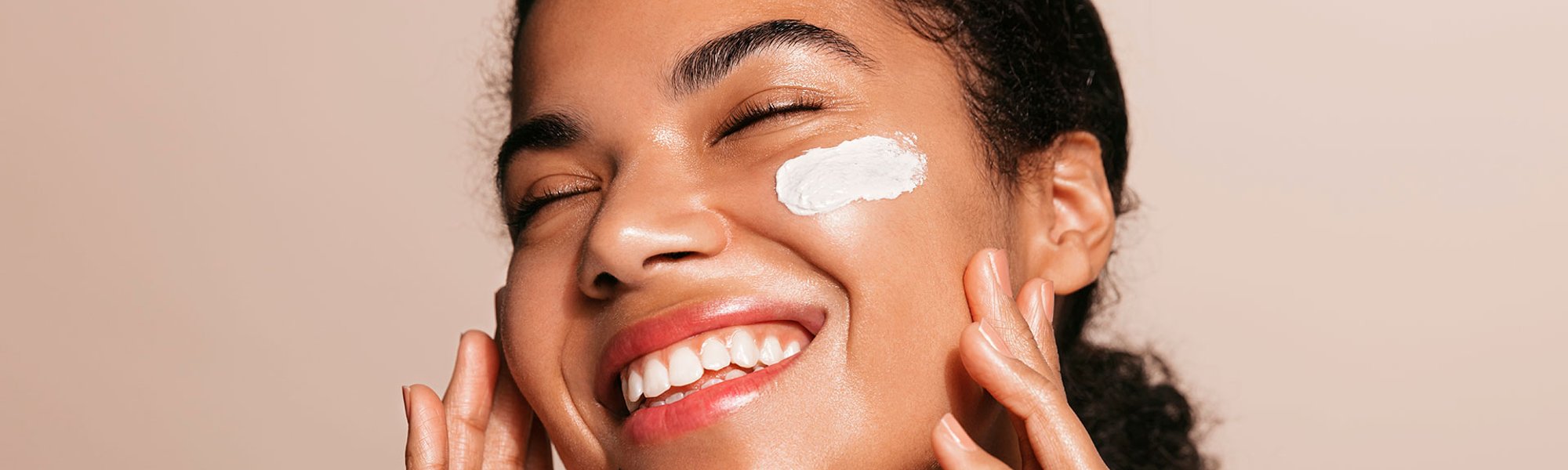 Mulher negra sorrindo com olho fechado e protetor solar facial aplicado na bochecha