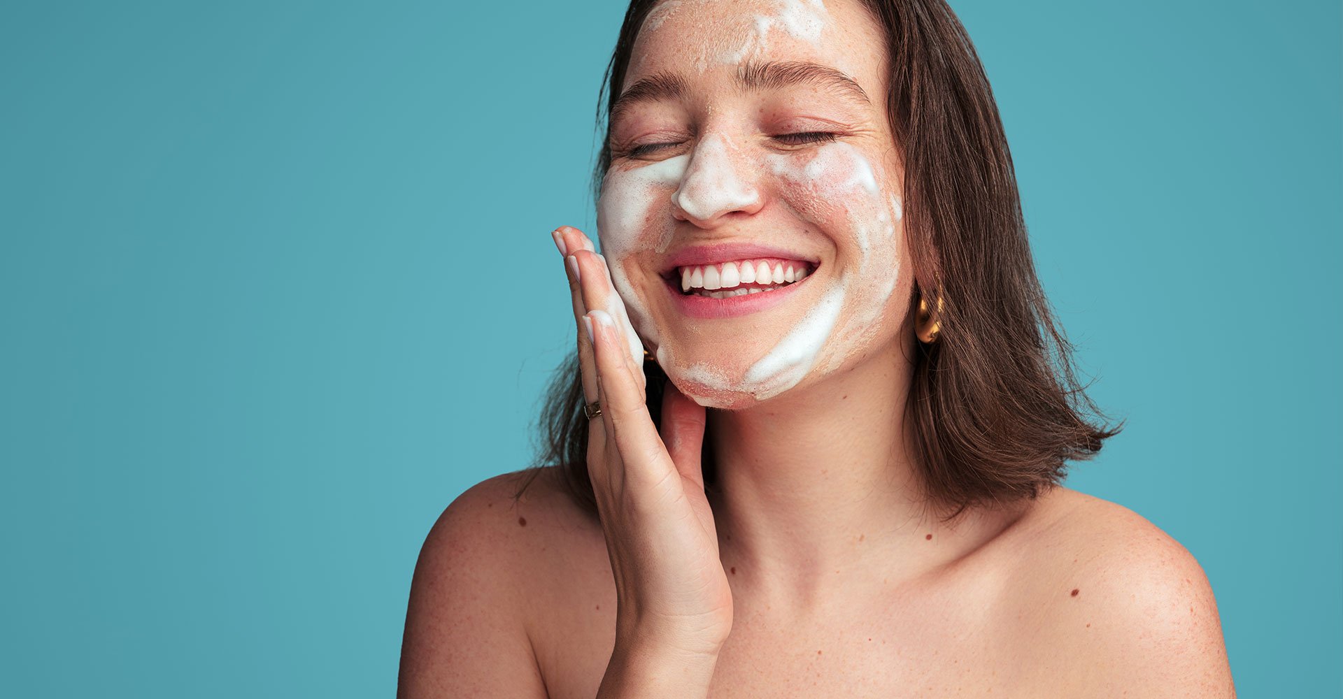 Mulher jovem sorri ao utilizar sabonete facial