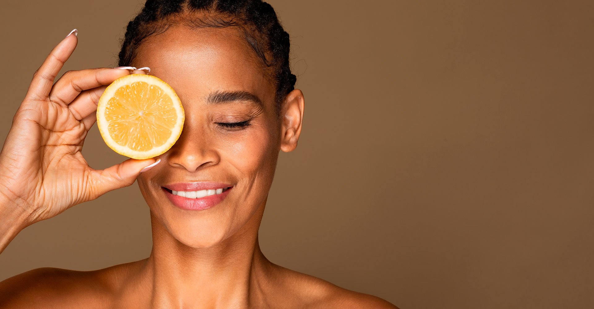 Mulher negra segurando uma laranja na altura dos olhos fazendo alusão ao uso da vitamina C no rosto