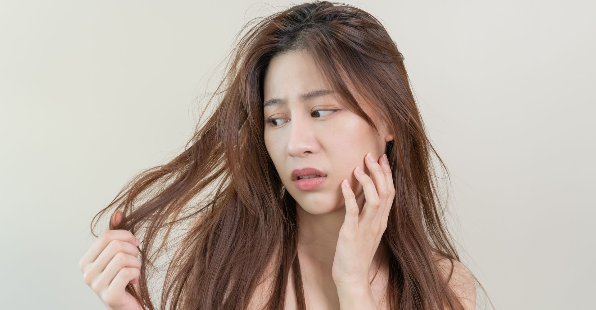 Mulher olhando com cara de preocupação enquanto encosta a mão no rosto olhando para o seu cabelo quebrado.