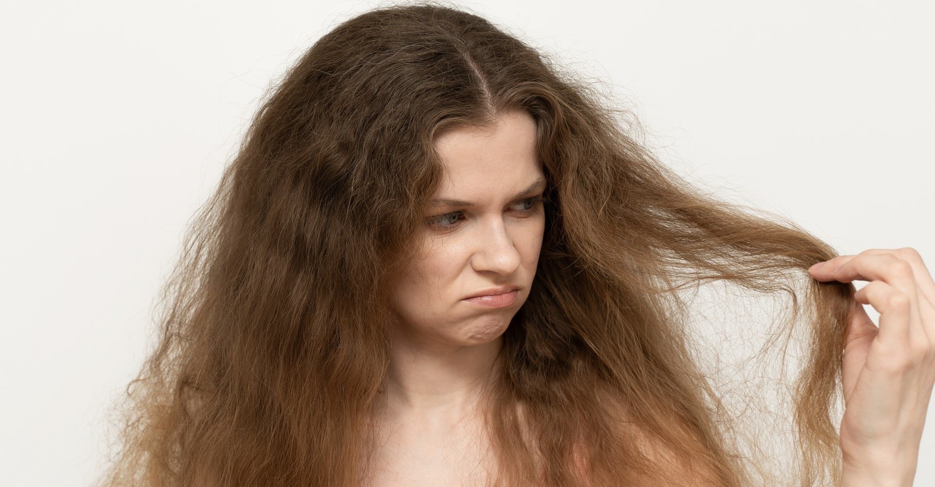 Menina olhando para o seu cabelo ressecado.