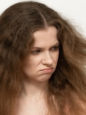 Menina olhando para o seu cabelo ressecado.