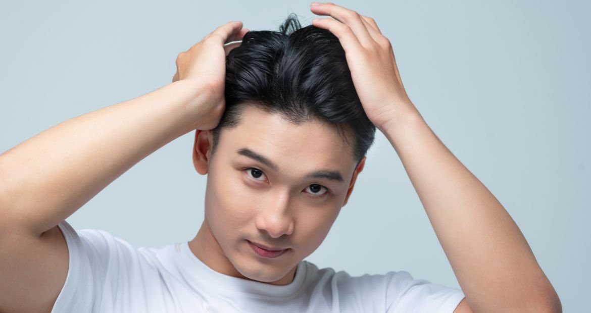 Homem asiático com as mãos no seu cabelo com corte social masculino.
