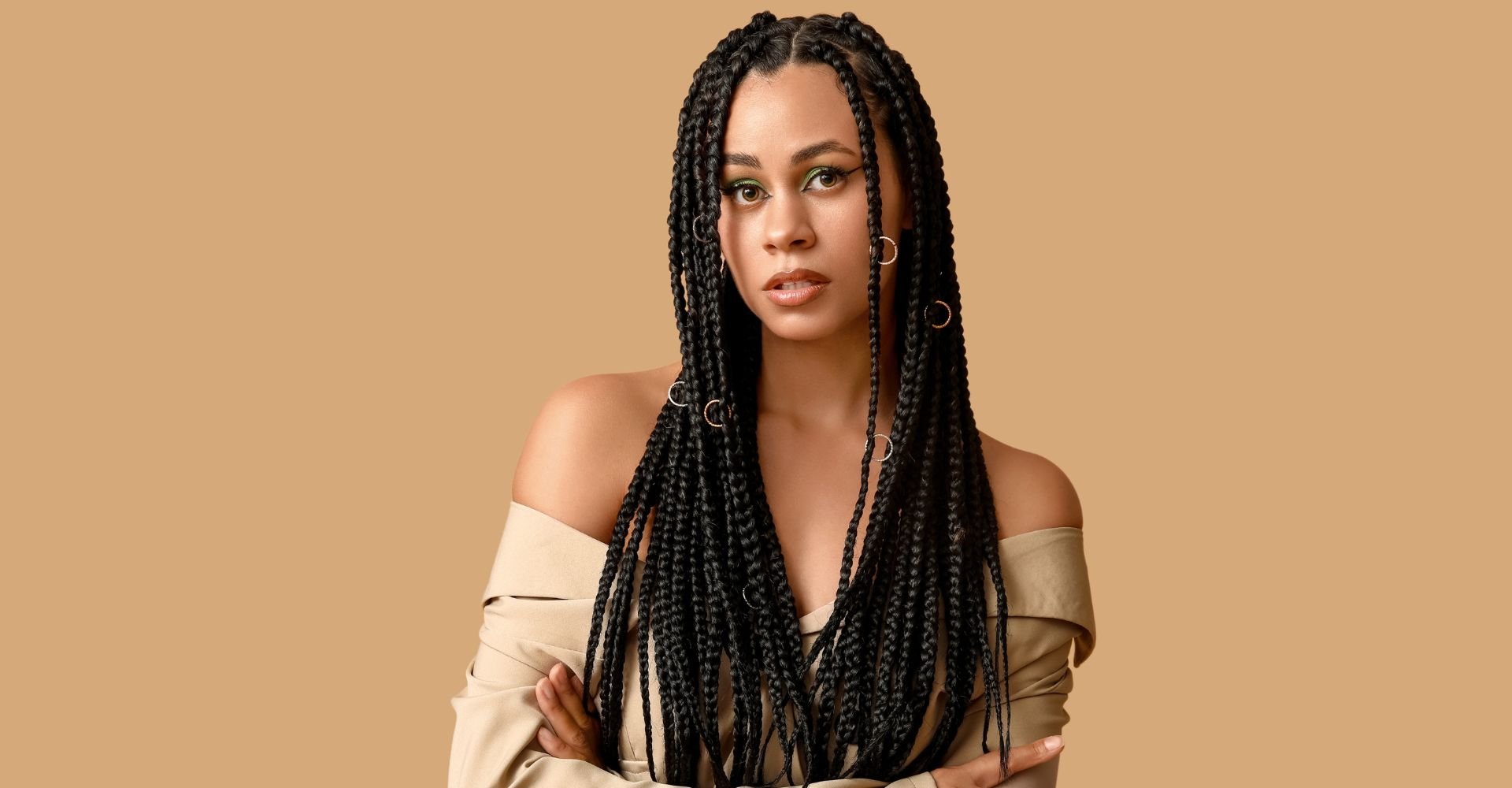 Mulher com os braços cruzados enquanto usa fulani braids no seu cabelo com argolas em algumas tranças.