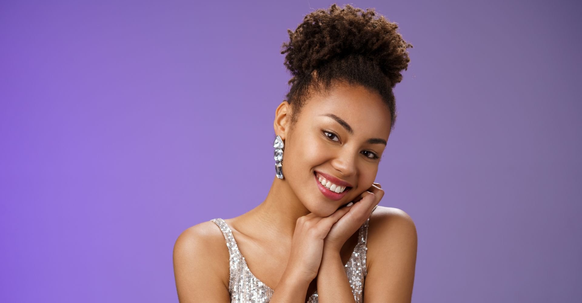 Mulher sorrindo com um coque alto e volumoso de cabelo crespo, ideal como penteado abacaxi para penteados para o fim do ano em cabelos cacheados.