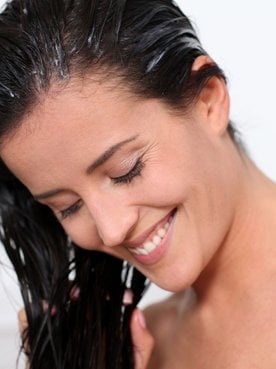 Mulher sorridente aplicando pré-shampoo nos seus fios úmidos.