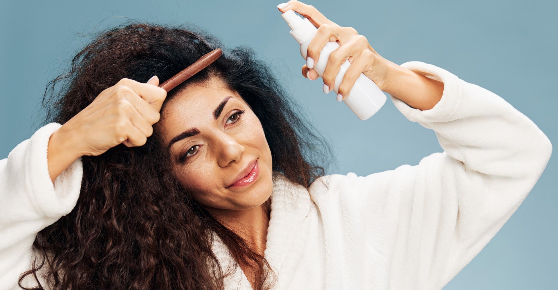Mulher penteando o cabelo enquanto aplica spray de cabelo.