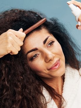 Mulher penteando o cabelo enquanto aplica spray de cabelo.