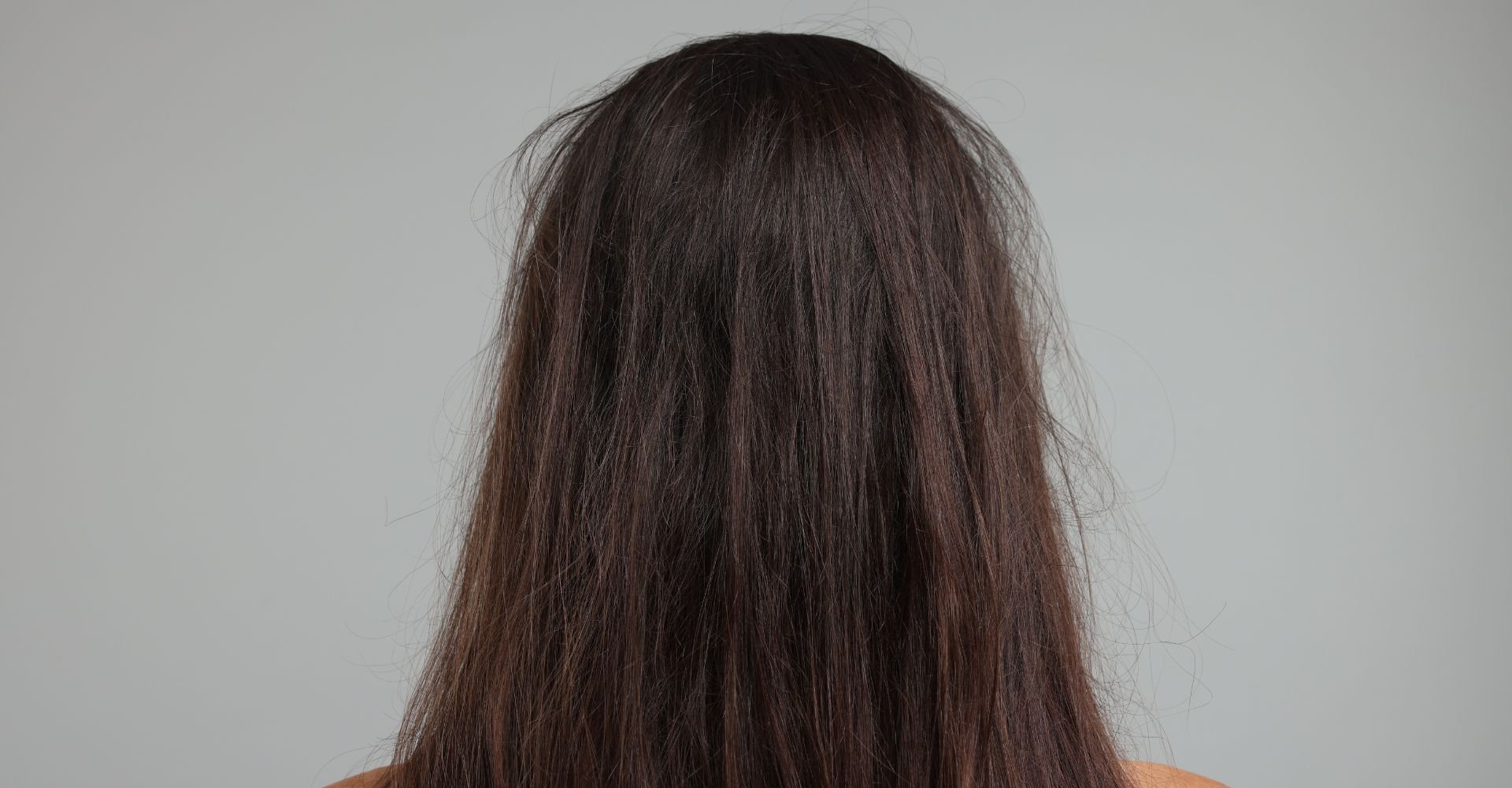 Mulher virada de costas com cabelo opaco com frizz em fundo cinza.