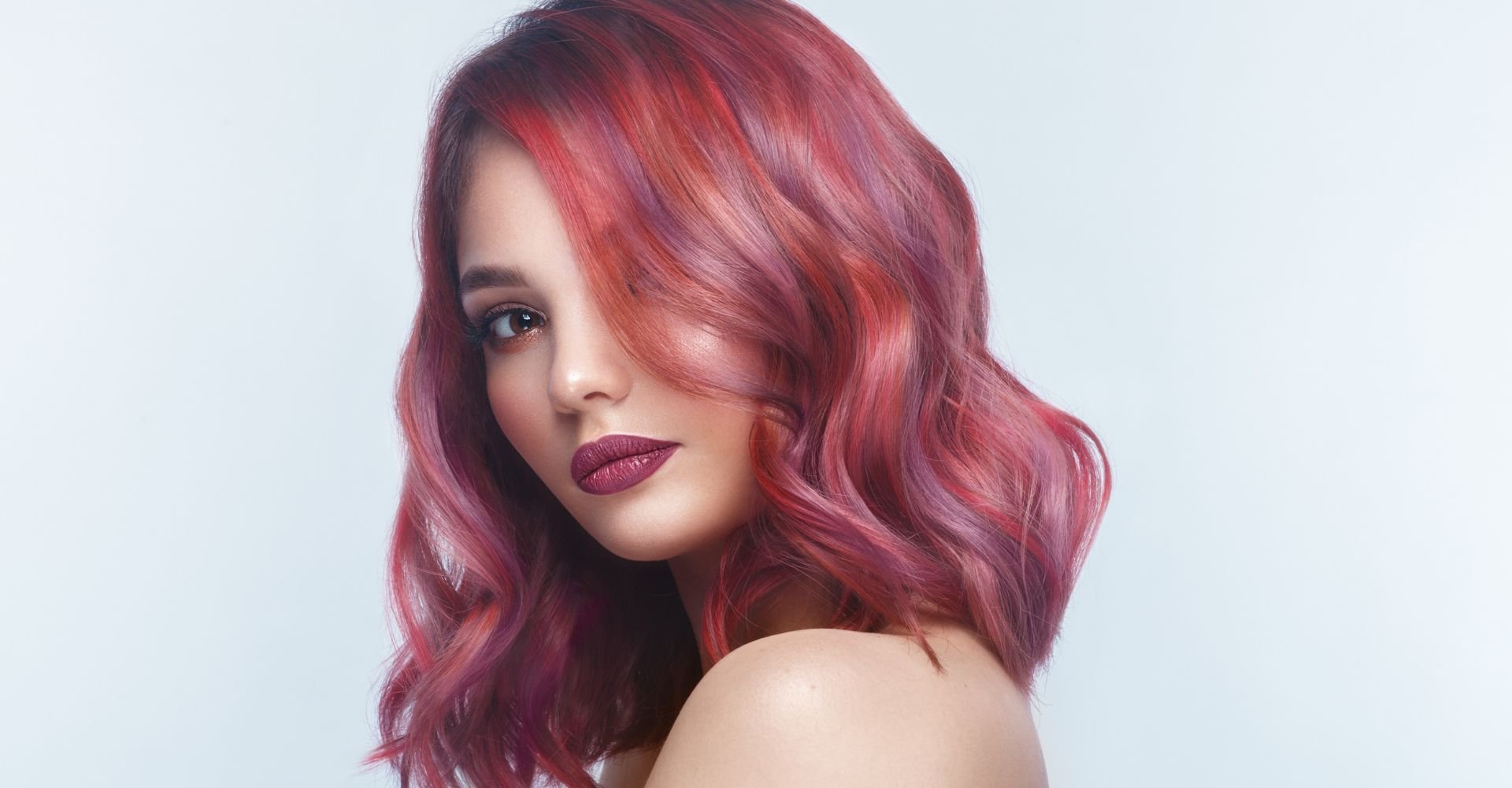 Cabelo médio ondulado em tom de vermelho vibrante com nuances rosadas, sobre fundo claro.