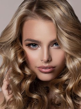 Mulher loira com os olhos azuis segurando seu cabelo com as duas mãos.