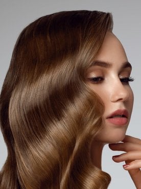 Mulher com cabelo loiro escuro com a mão no queixo.