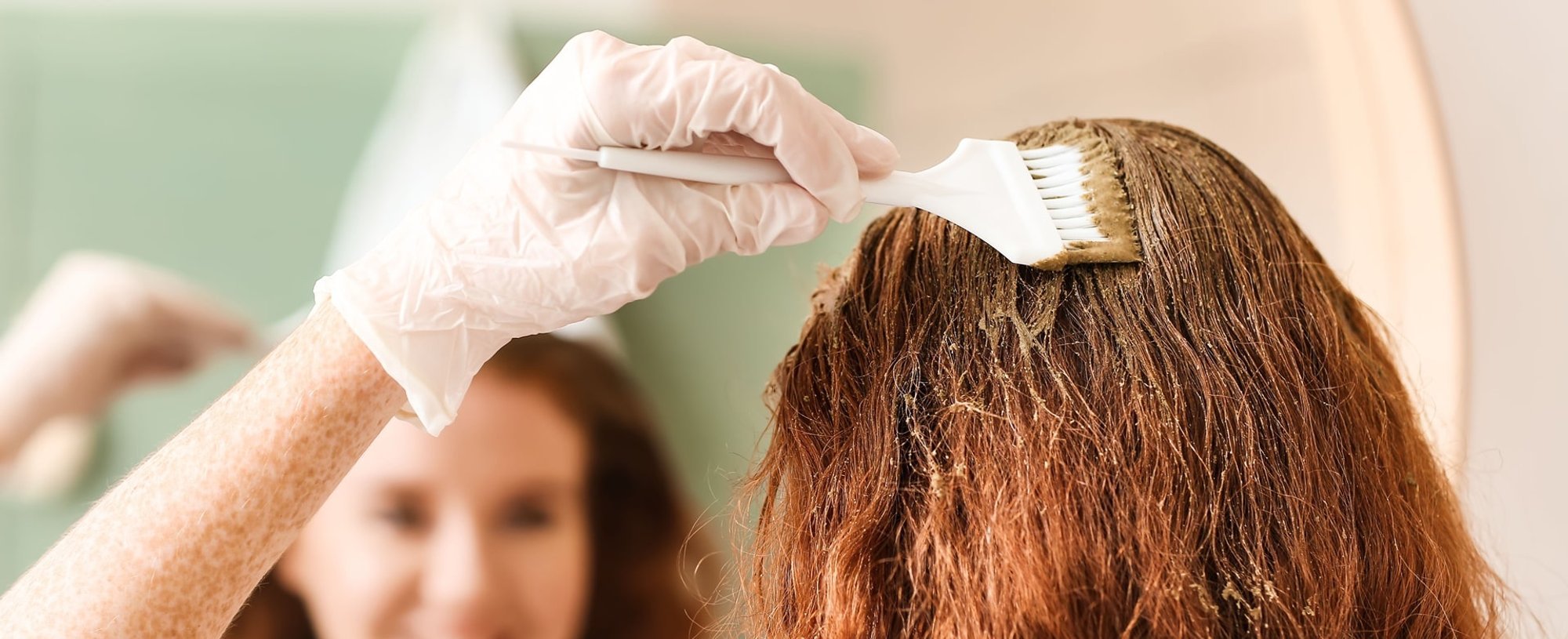 Mulher ruiva pintando o cabelo em casa com tintura sem amônia.