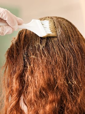 Mulher ruiva pintando o cabelo em casa com tintura sem amônia.