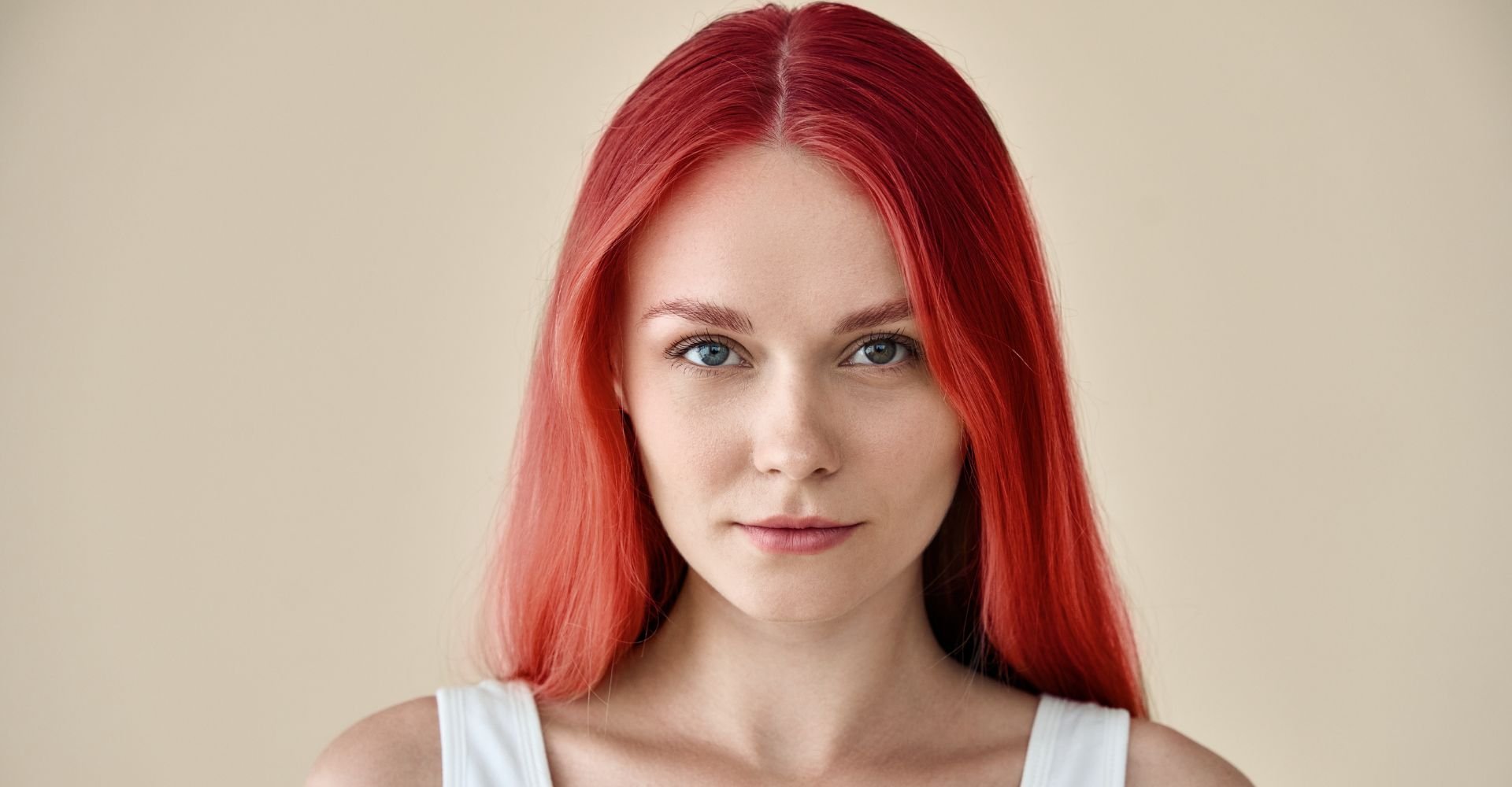 Mulher olhando para a câmera usando uma regata branca com cabelo vermelho após passar um tonalizante vermelho.
