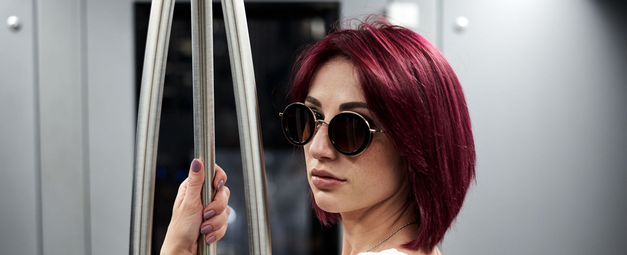 Mulher com cabelo na cor vermelho borgonha olhando para trás enquanto segura em um lugar para ficar em pé no metrô.