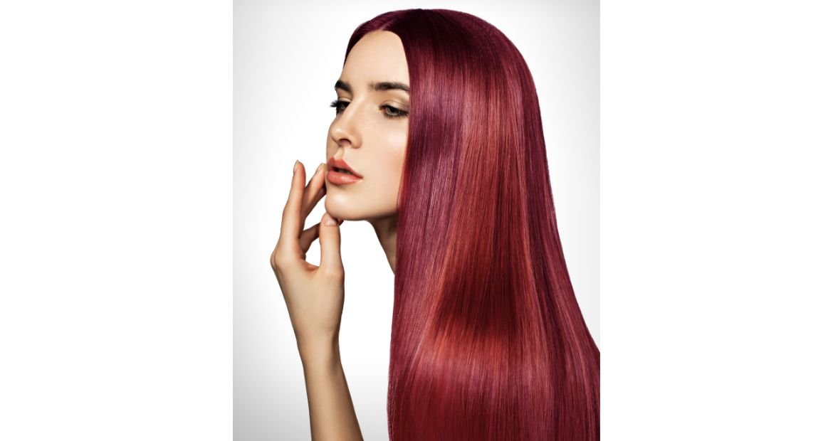 Mulher com a mão no rosto e cor de cabelo vermelho borgonha nos fios.