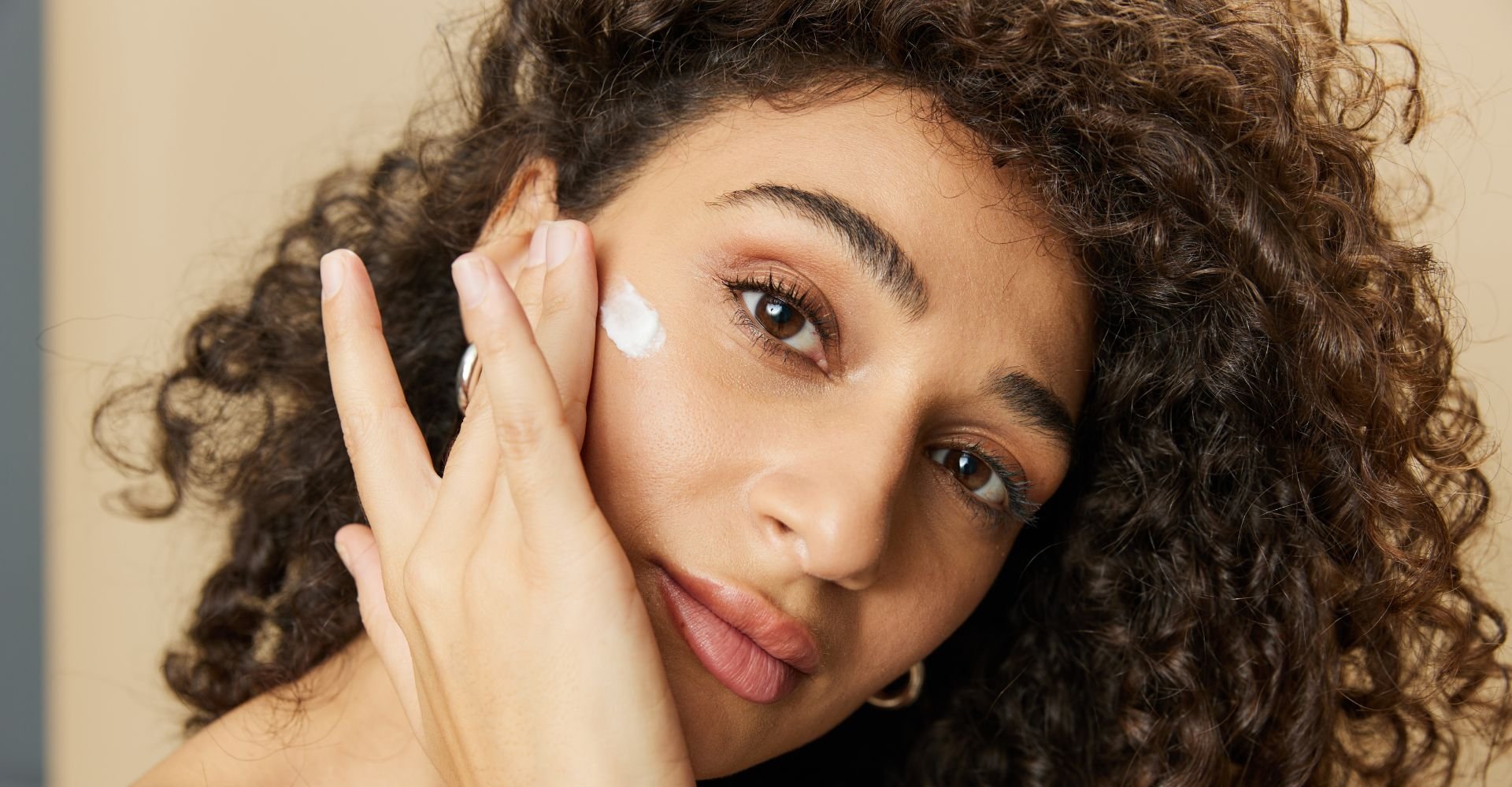 Jovem mulher negra aplica creme facial em sua pele do rosto para hidratar e tratar