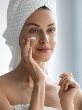 Mulher passando creme facial noturno no rosto.