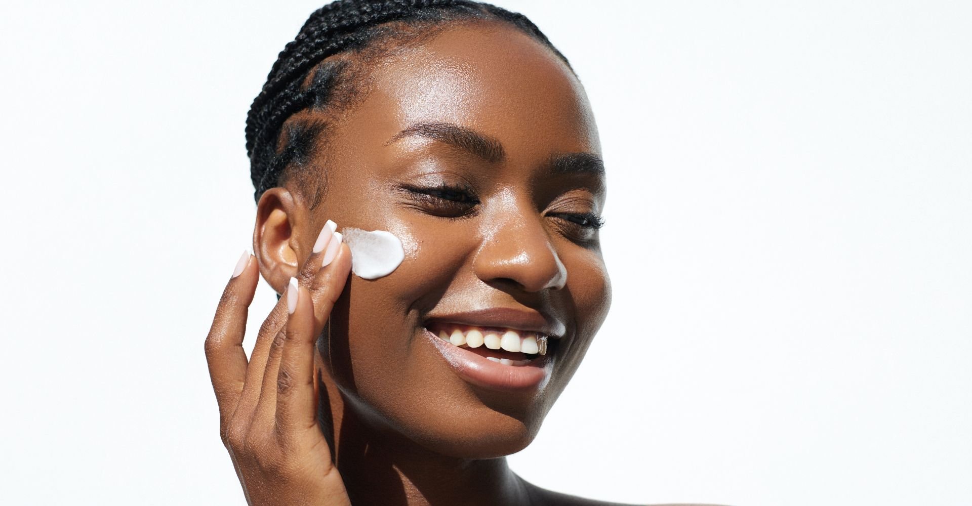 Jovem mulher negra sorridente aplica creme hidratante em sua pele facial
