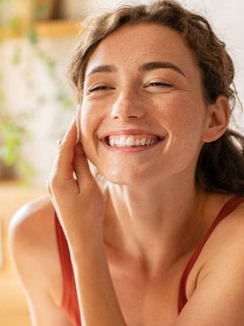 Mulher sorridente passando algodão no rosto para limpar sua pele.