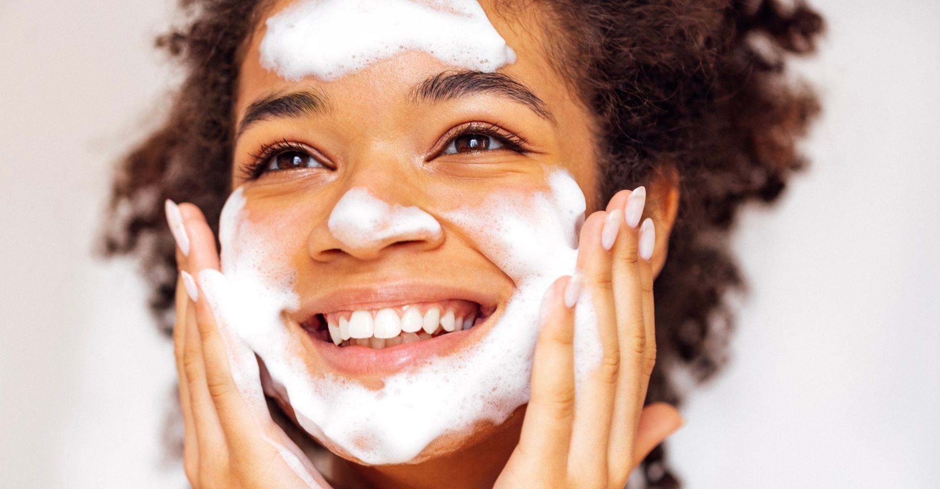 Jovem negra sorridente ao utilizar a espuma de limpeza facial 