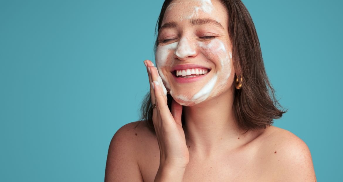 Jovem branca e sorridente aplicando a espuma de limpeza para o rosto em sua pele facial 