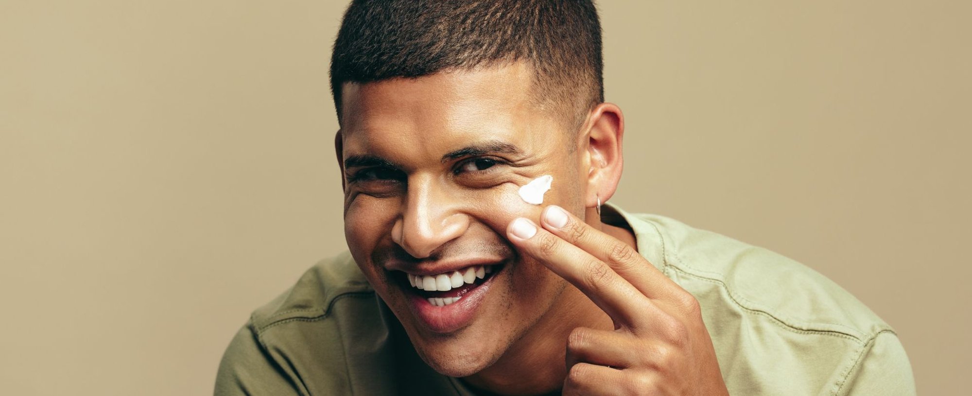 Jovem aplica um hidratante masculino em seu rosto como parte do skincare masculino